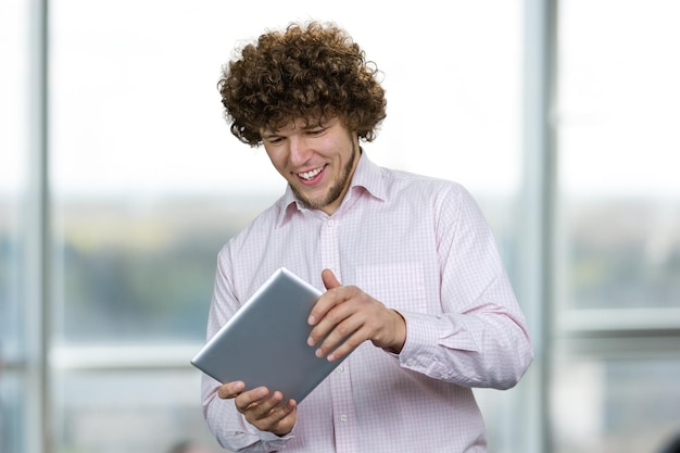 Photo portrait d'un jeune homme caucasien heureux aux cheveux bouclés jouant à un jeu vidéo sur la tablette