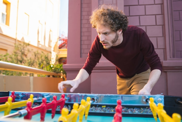 Portrait de jeune homme caucasien s'amusant et jouant au baby-foot.