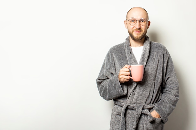 Portrait d'un jeune homme chauve avec une barbe dans une robe de chambre et des verres tenant une tasse de café