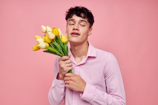 Portrait d'un jeune homme en chemise rose avec un bouquet de fleurs faisant des gestes avec ses mains