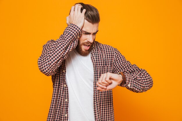 Portrait d'un jeune homme choqué portant des vêtements décontractés vérifiant sa montre intelligente