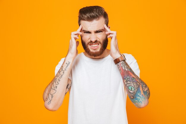 Portrait d'un jeune homme en colère portant des vêtements décontractés debout isolé sur mur jaune, hurlant, souffrant d'un mal de tête