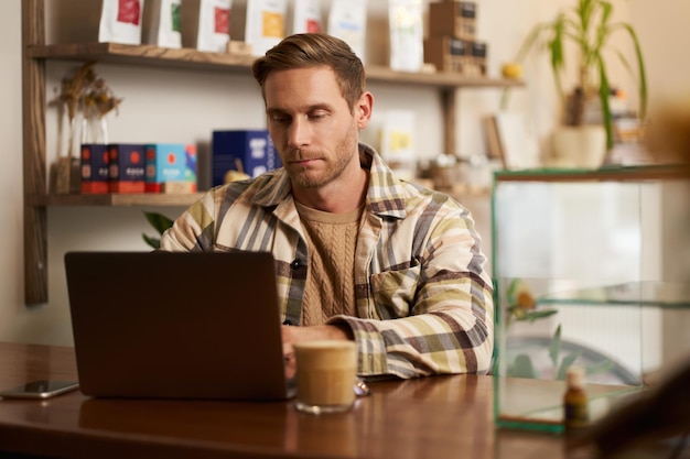 Portrait d'un jeune homme concentré travaillant sur un ordinateur portable, un pigiste faisant son projet dans un café.