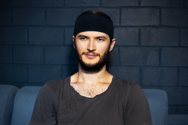 Portrait de jeune homme confiant assis sur un canapé, sur fond de mur de briques noires.