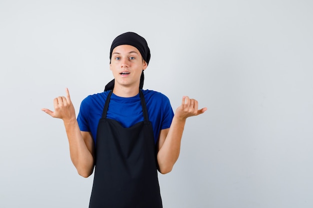 Portrait d'un jeune homme cuisinier montrant un geste de téléphone en t-shirt, tablier et regardant la vue de face hésitante