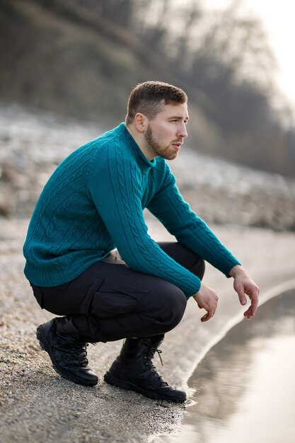 Portrait d'un jeune homme dans un pull turquoise debout près de la rivière