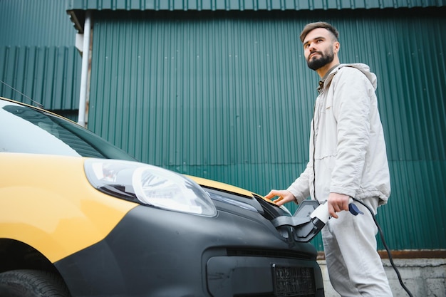 Portrait d'un jeune homme debout avec un câble de charge près de la station de charge