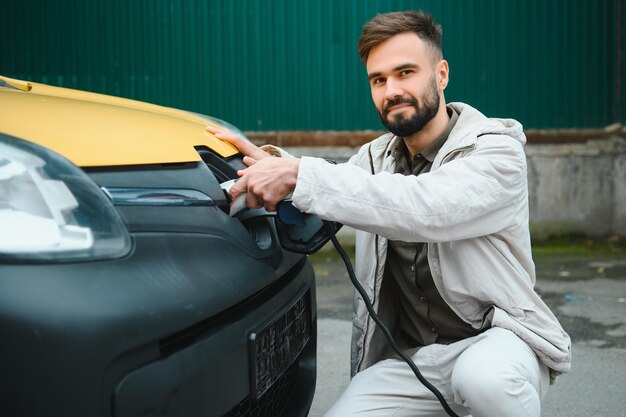 Portrait d'un jeune homme debout avec un câble de charge près de la station de charge