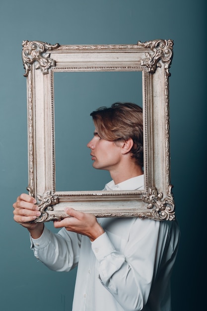 Portrait jeune homme debout avec cadre photo au studio.