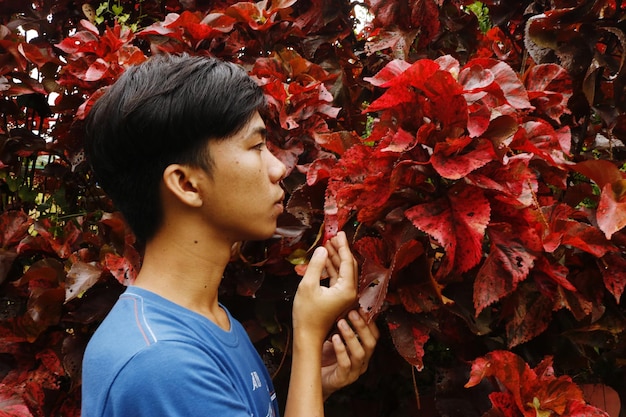 Photo portrait d'un jeune homme debout près des feuilles d'acalypha en automne