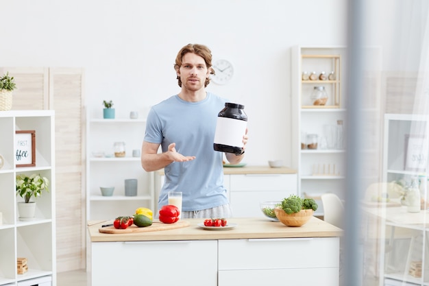 Portrait de jeune homme debout à la table avec des légumes frais et pointant sur une bouteille avec une bonne nutrition