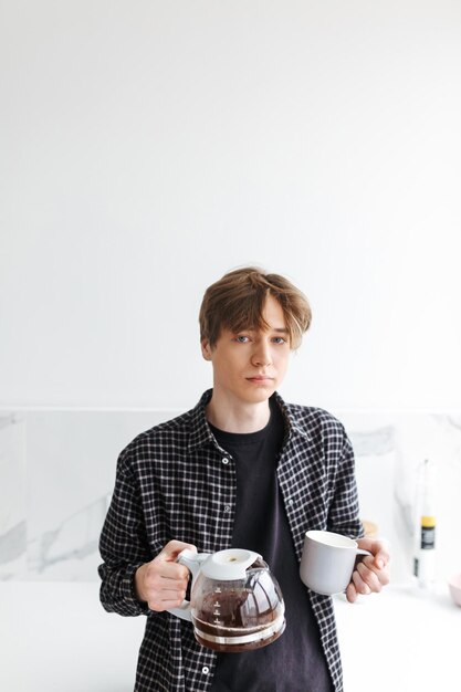 Portrait de jeune homme debout et versant du café tout en regardant à huis clos à la maison