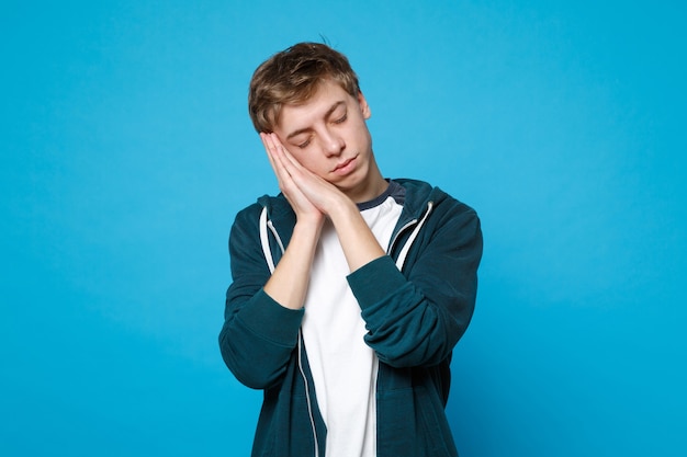 Portrait D'un Jeune Homme Détendu En Vêtements Décontractés, Gardant Les Yeux Fermés, Se Reposant, Dormant Avec Les Mains Près Du Visage Isolé Sur Le Mur Bleu. Concept De Mode De Vie Des émotions Sincères Des Gens.