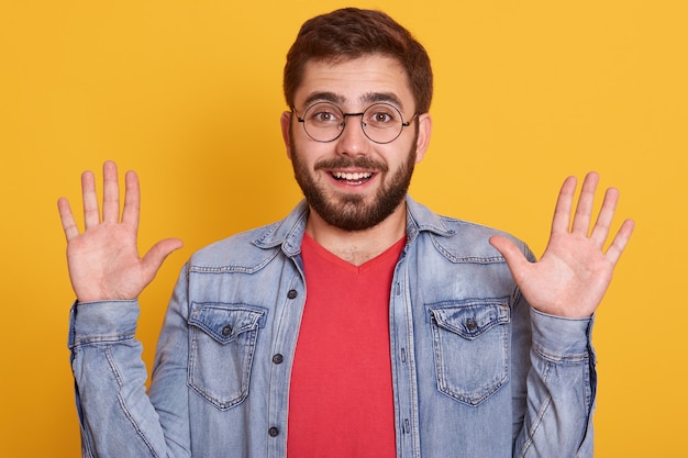 Portrait de jeune homme excité à la recherche avec une expression étonnée et levant les bras, chemise rouge habillée et veste en jean