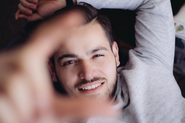 Portrait d'un jeune homme faisant un cadre à doigts à la maison
