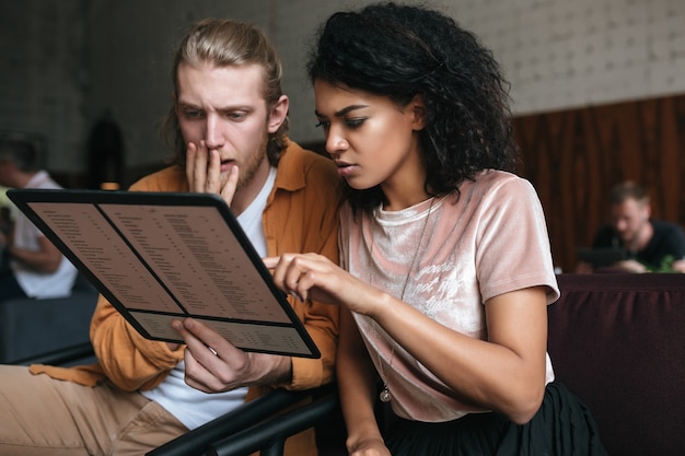 Portrait de jeune homme et femme assise au restaurant avec menu en mains