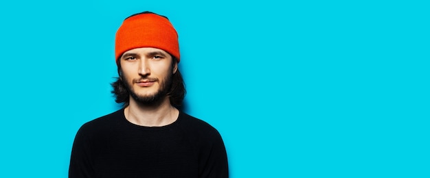 Photo portrait de jeune homme sur fond bleu, portant un chapeau orange et un pull noir. vue panoramique de la bannière avec espace de copie.