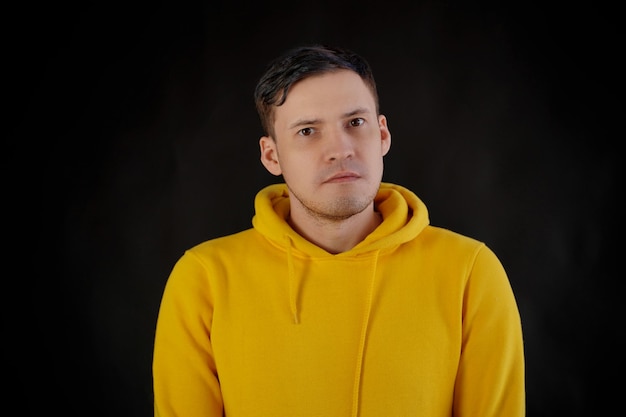 Portrait de jeune homme sur fond noir Beau mec en sweat à capuche jaune posant sur fond sombre