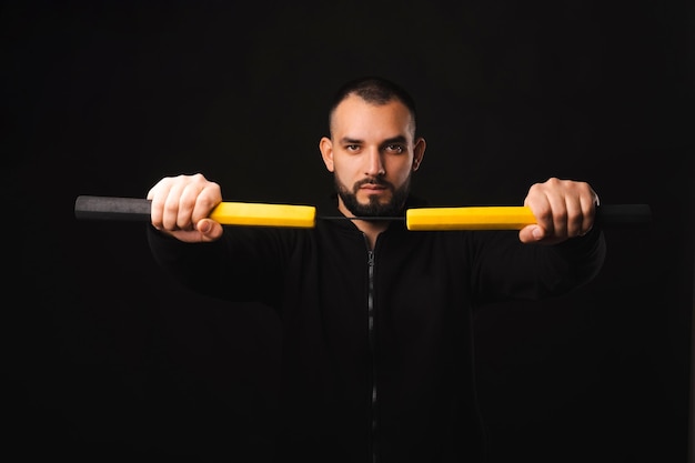 Portrait d'un jeune homme fort tenant un nunchaku et regardant la caméra sur fond sombre