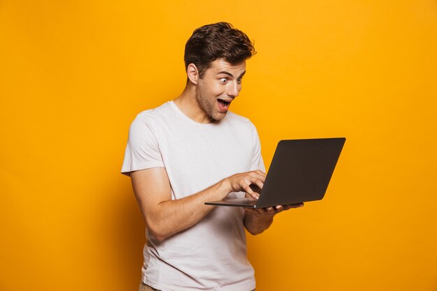 Portrait d'un jeune homme gai à l'aide d'un ordinateur portable