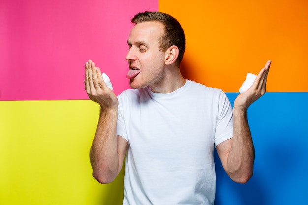 Portrait d'un jeune homme gai sur fond multicolore, vêtu d'un T-shirt blanc, a versé de la mousse pour les cheveux dans ses mains, crée une coiffure à la mode