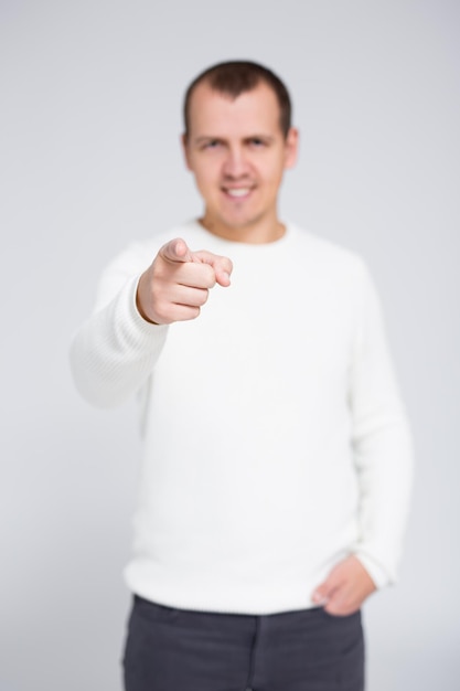 Portrait de jeune homme gai pointant son doigt vers vous sur fond gris