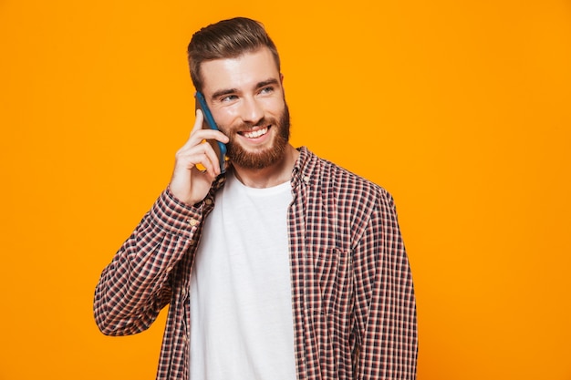 Portrait d'un jeune homme gai portant des vêtements décontractés parlant au téléphone mobile