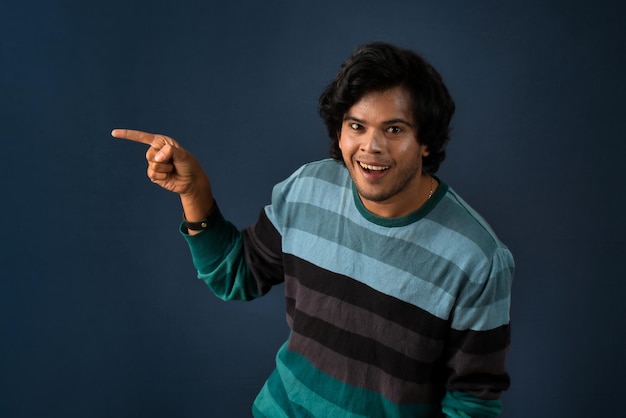 Portrait d'un jeune homme gai réussi pointant et présentant quelque chose avec la main ou le doigt avec un visage souriant heureux