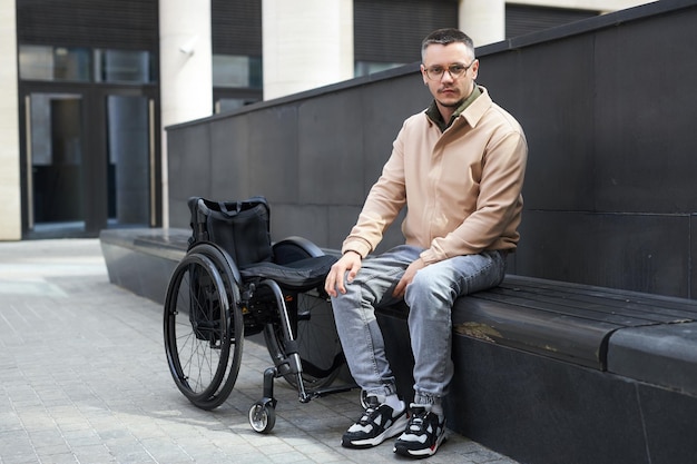 Portrait de jeune homme handicapé regardant la caméra assis sur un banc à l'extérieur