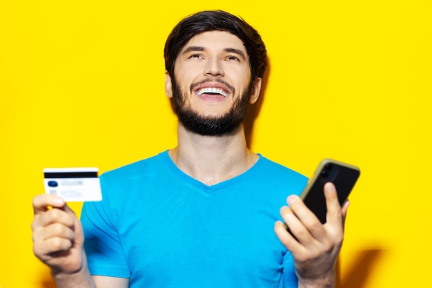 Portrait de jeune homme heureux à l'aide de smartphone et carte de crédit sur la couleur jaune