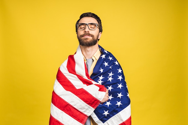 Portrait de jeune homme heureux barbu tenant un drapeau américain USA isolé sur fond jaune.