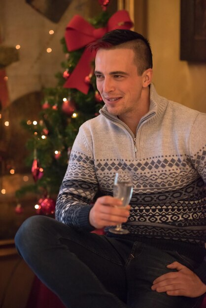 Portrait d'un jeune homme heureux avec une coupe de champagne célébrant les vacances d'hiver à la maison joliment décorée pour Noël