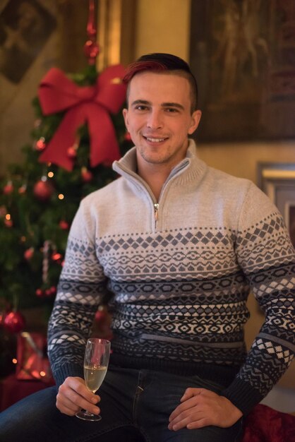 Portrait d'un jeune homme heureux avec une coupe de champagne célébrant les vacances d'hiver à la maison joliment décorée pour Noël