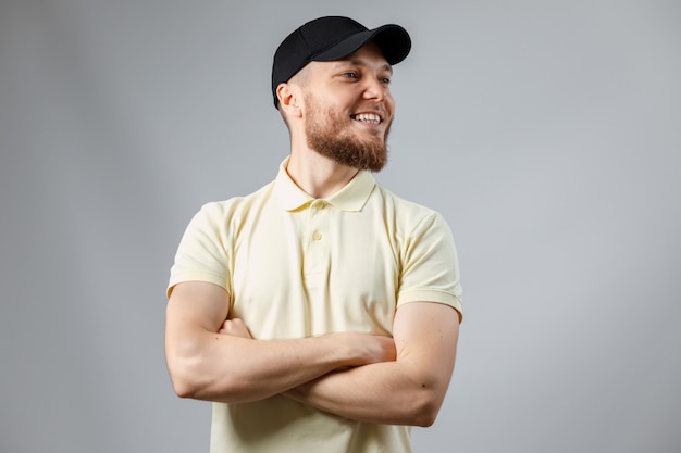 Portrait d'un jeune homme heureux dans un T-shirt jaune et une casquette noire détourne le regard sur le gris.