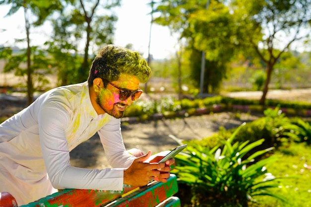 Portrait d'un jeune homme heureux indien sur le festival de couleurs holi à l'aide d'un téléphone portable