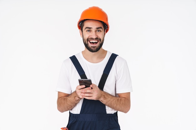 Portrait d'un jeune homme heureux et positif en casque posant isolé sur un mur blanc à l'aide d'un téléphone portable.