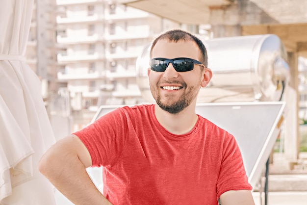 Portrait de jeune homme heureux sourires millénaires portant des lunettes de soleil et un t-shirt rouge le jour d'été ensoleillé