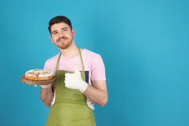 Portrait de jeune homme heureux tenant un gâteau frais et gesticulant le pouce vers le haut.