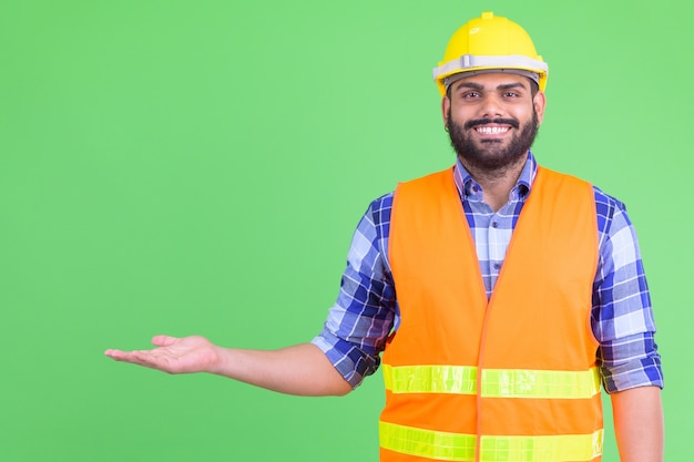 Portrait de jeune homme indien barbu en surpoids construction worker contre chroma key avec mur vert