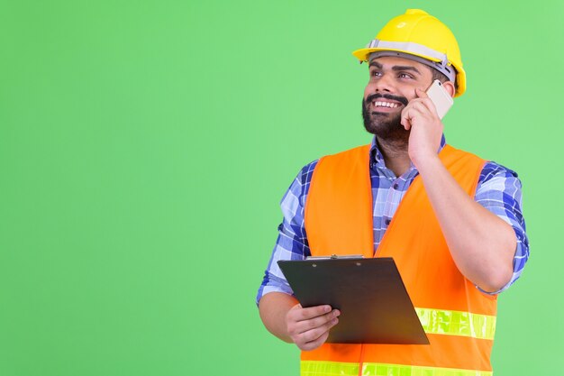 Portrait de jeune homme indien barbu en surpoids construction worker contre chroma key avec mur vert