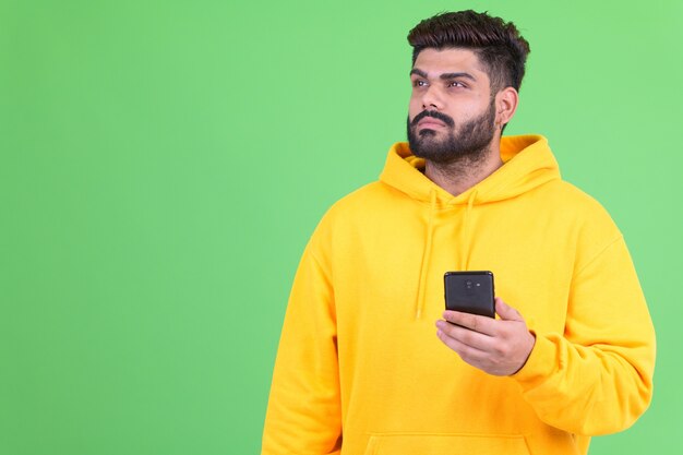 Portrait de jeune homme indien barbu en surpoids portant un sweat à capuche contre chroma key avec mur vert