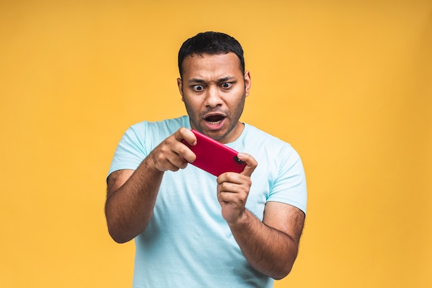 Portrait d'un jeune homme indien noir africain joyeux vêtu de jeux occasionnels sur téléphone portable isolé sur fond jaune.