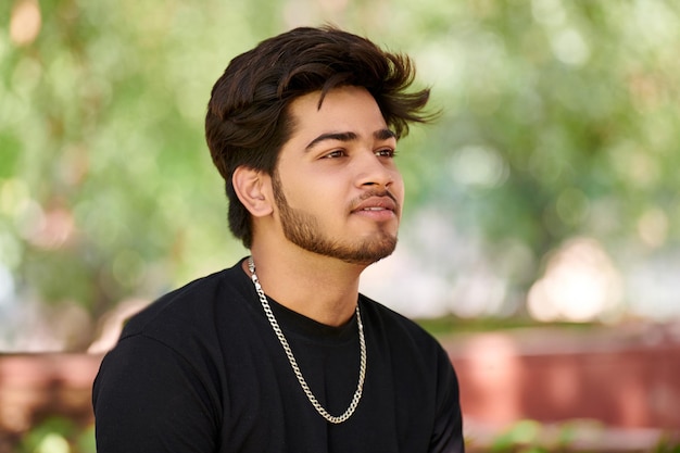 Portrait de jeune homme indien séduisant en t-shirt noir et chaîne de cou en argent sur fond de parc verdoyant