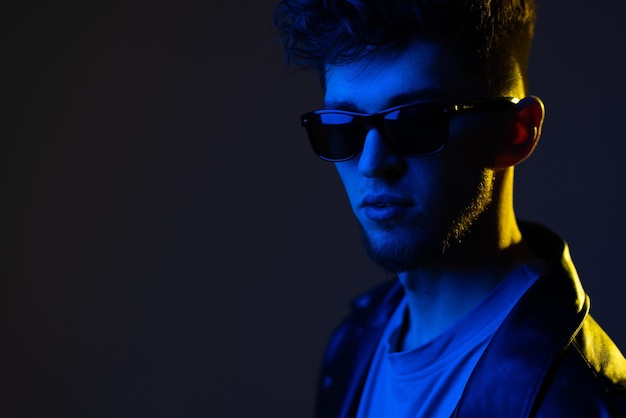Portrait de jeune homme isolé sur fond de studio bleu en néon Beau modèle masculin en vêtements de cuir Concept d'émotions humaines annonce de vente d'expression faciale