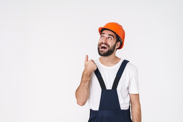 Portrait d'un jeune homme joyeux et heureux en casque posant isolé sur un mur blanc pointant de côté.