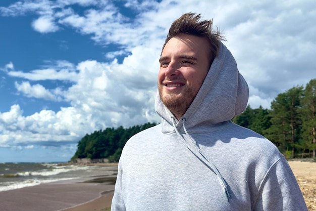 Portrait d'un jeune homme joyeux et joyeux à pied à l'extérieur sur la plage en été ou en automne se détendre