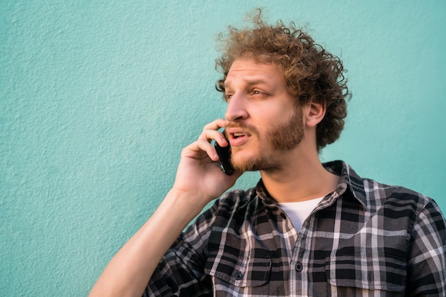 Portrait de jeune homme latin parlant au téléphone contre l'espace bleu clair. Concept de communication.