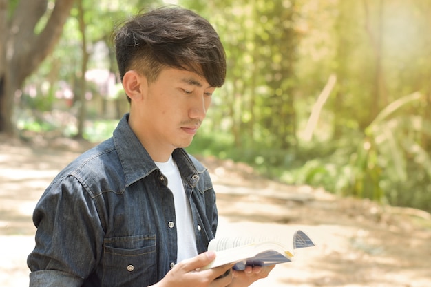 Portrait de jeune homme lisant un livre dans le parc le jour de l'été.