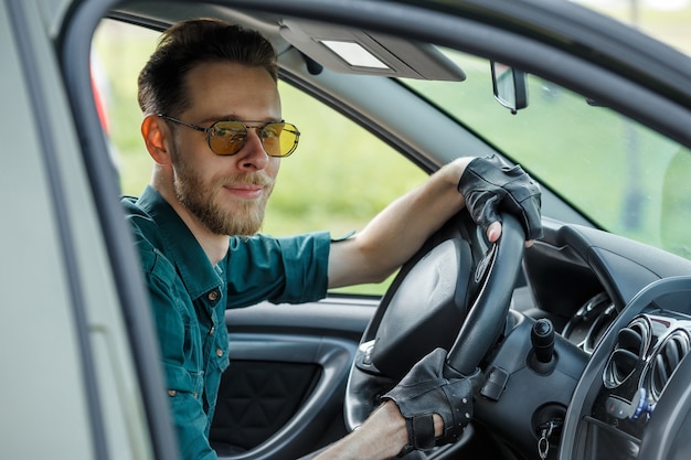 Portrait d'un jeune homme à lunettes noires au volant d'une voiture