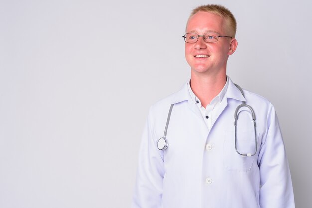 Portrait de jeune homme médecin aux cheveux blonds portant des lunettes contre le mur blanc